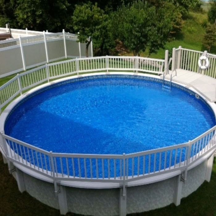 A circular above-ground pool with clear blue water is enclosed by the FENCE AG 24IN RESIN C TAUPE safety fence, featuring a deck and ladder. Green trees and grass can be seen in the background.