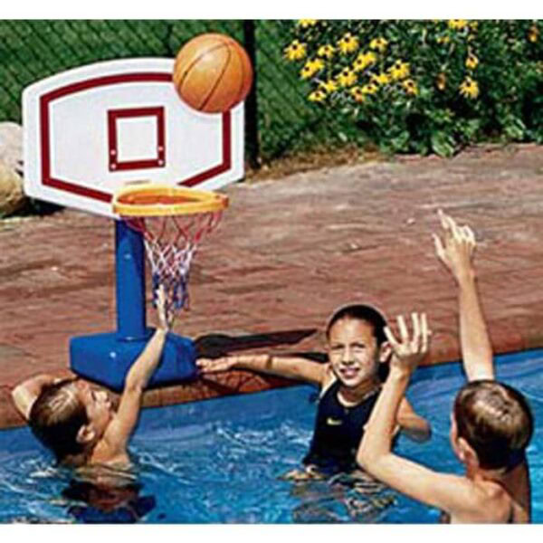 Three kids play basketball in a pool, aiming to score in the Jammin Deck Basketball Game hoop set up at the pool’s edge. Yellow flowers and green foliage can be seen behind them.