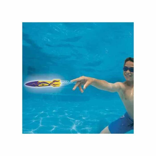 A boy in swim goggles and blue trunks is underwater in a pool, launching a Toypedo Bandits—a small, colorful torpedo-shaped toy that zooms forward and leaves a trail of bubbles.