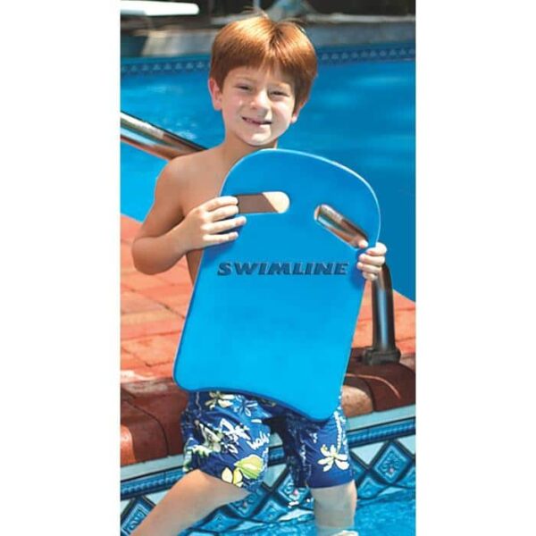 A young boy in blue floral swim trunks stands by the pool, smiling at the camera while holding an Aqua-Coach Foam Kickboard.
