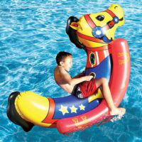 A young boy in swim trunks rides the ROCKING HOBBY HORSE POOL&LAWN inflatable in a clear blue pool, smiling and splashing water with his foot.