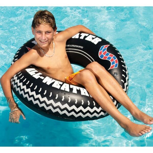 A smiling boy relaxes in a swimming pool, sitting in the 36 Momster Tire Ring inflatable tube, wearing orange swim trunks.