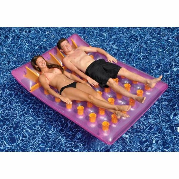 A woman and a man in swimsuits relax on a Double French Mattress—a pink inflatable pool float with cup holders—floating on clear blue water.