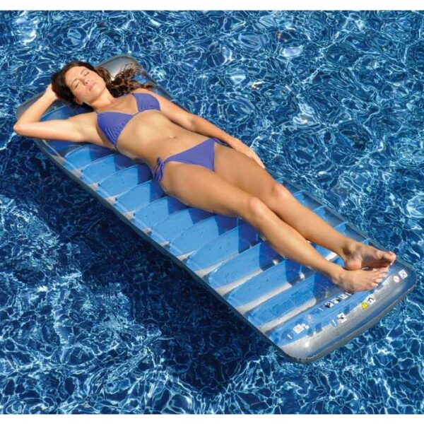 A woman in a blue bikini is sunbathing with her eyes closed on the Deluxe Suntanner Mattress, a transparent inflatable pool float, enjoying a bright, sunny day in a swimming pool with clear blue water.