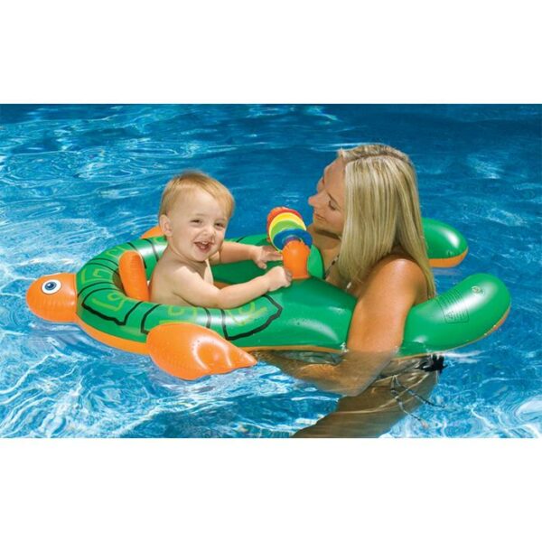 A smiling woman holds a happy toddler in the Me & You Baby Seat, a green inflatable turtle float, in a swimming pool. The toddler faces her and grips the float’s handles, both enjoying their time in the water.