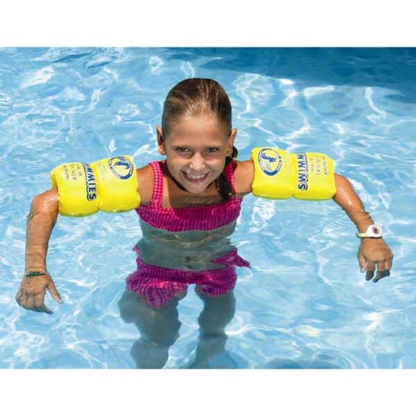 A smiling girl with brown hair in a ponytail wears Aqua-Coach SkillSchool™ Swimmies and a pink swimsuit while standing in a swimming pool.