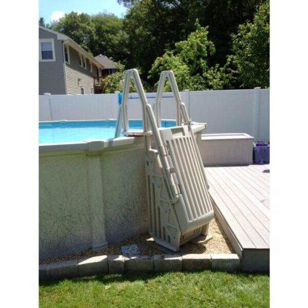 A Deluxe Step Entry with Gate is folded and locked outside an above-ground pool beside a wooden deck and white fence, with grass and trees visible in the background.