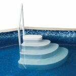 The Step In A Box features white plastic pool steps with a handrail, designed for above-ground pools. Its curved, perforated steps descend gradually into the water, offering safe and easy access while reflecting in the blue pool.