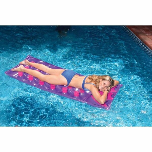 A woman smiles and relaxes, lying on her stomach on a French Pocket Mattress, floating in a clear blue swimming pool.