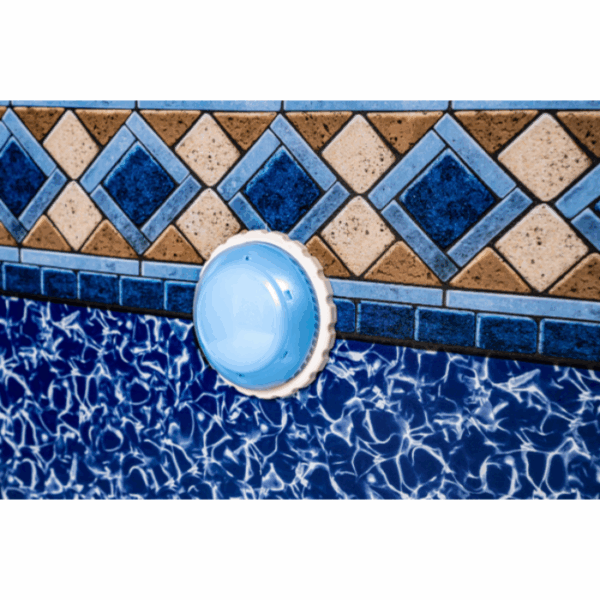 A close-up of the LIGHT-ARIES SMART LED AG, a blue and white pool fitting, installed on a swimming pool’s patterned tile wall with geometric blue, brown, and tan designs above a water-like wave pattern.