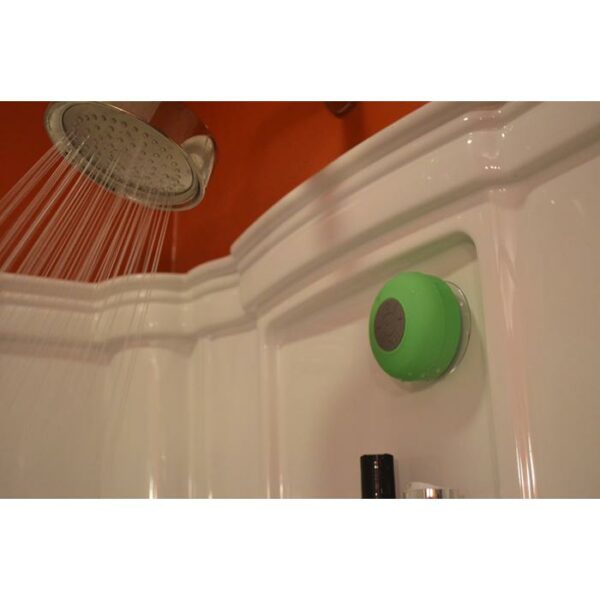A showerhead sprays water in a white stall, with the SOUNDWAVES-OUTDOOR SPEAKER—a green waterproof Bluetooth speaker—attached to the wall nearby.