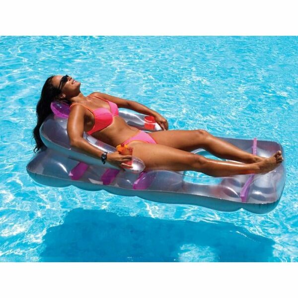 A woman in a pink bikini and sunglasses relaxes on a Deluxe Lounge Chair, floating on bright blue water under the sun while holding a drink.