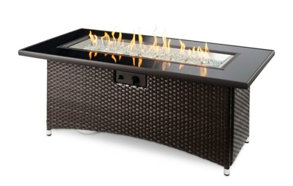 The Montego Firepit Table features a rectangular design with a dark woven rattan base and a glass-covered central fire feature, displaying flames above decorative stones.