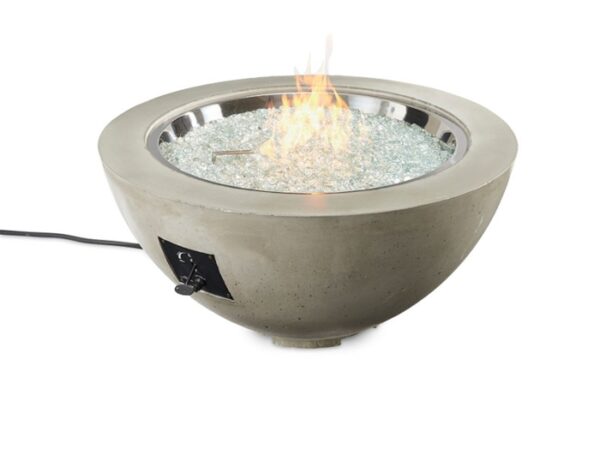 The Cove Gas Firepit Bowl 30 features a modern round design with a smooth concrete finish, clear glass rocks, and a central flame. An ignition switch and power cord are located on the side for easy operation.