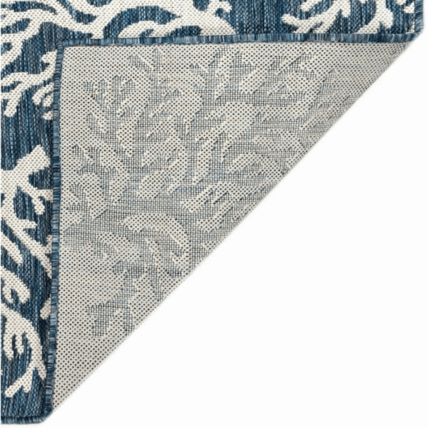 The Outdoor Rug-Coral Border Navy is shown with one corner flipped to display its non-slip backing and a faded version of the coral border design on the underside.