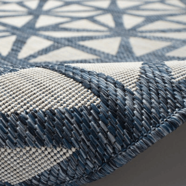 Close-up of the Outdoor Rug-Tonga Tile Navy, featuring a blue and white geometric, star-like pattern. The slightly curled edge highlights the textured weave and intricate detailing of this durable outdoor rug.