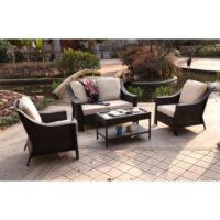 The Bray 4 PC Wicker Collection features cream cushions and a coffee table with decor, arranged on a paved patio near a pond and wooden bridge in a landscaped garden.
