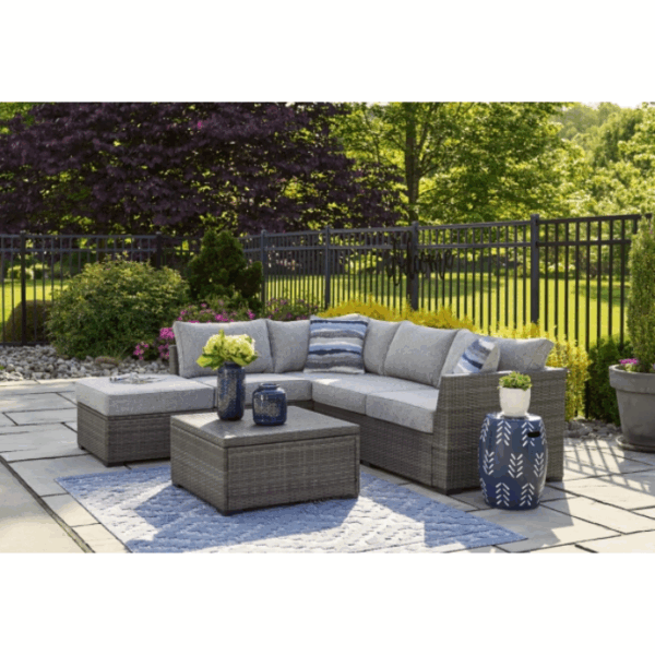 Outdoor patio featuring the Petal Road Grouping 4-Piece gray wicker sectional with gray cushions, blue-and-white striped pillows, matching coffee table, blue vases, potted plants on a blue rug, surrounded by fencing and greenery.