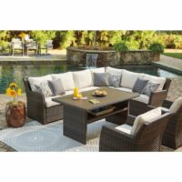 The Easy Isle 5-Piece Grouping, featuring wicker furniture with cream cushions and patterned pillows, is arranged on a rug beside a pool with waterfall. A table holds orange juice, while a side table displays sunflowers in a vase.