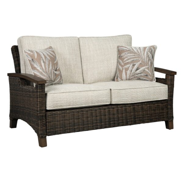 The Paradise Trail Grouping (3 pc) features a wicker loveseat with light beige cushions, two leaf-patterned pillows, wooden armrests, and a sturdy frame.
