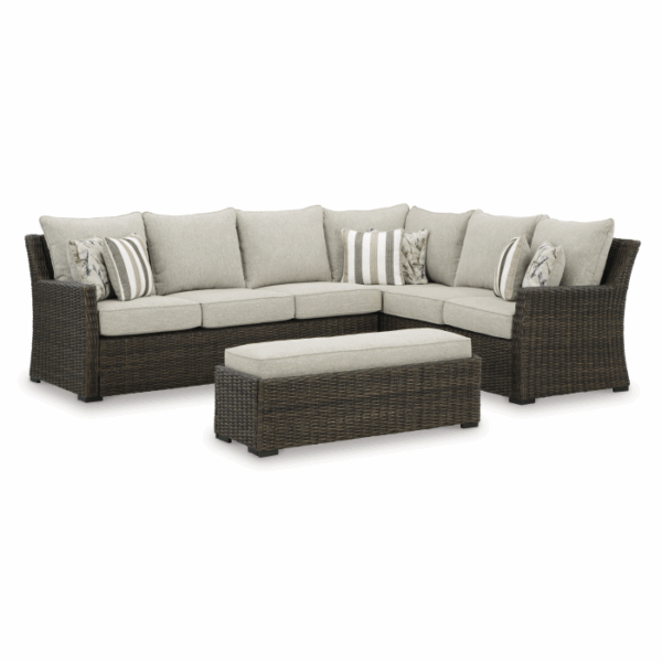The Brook Ranch Grouping 4-Piece features a dark wicker outdoor sectional sofa with beige cushions, two striped accent pillows, and a matching rectangular wicker ottoman.