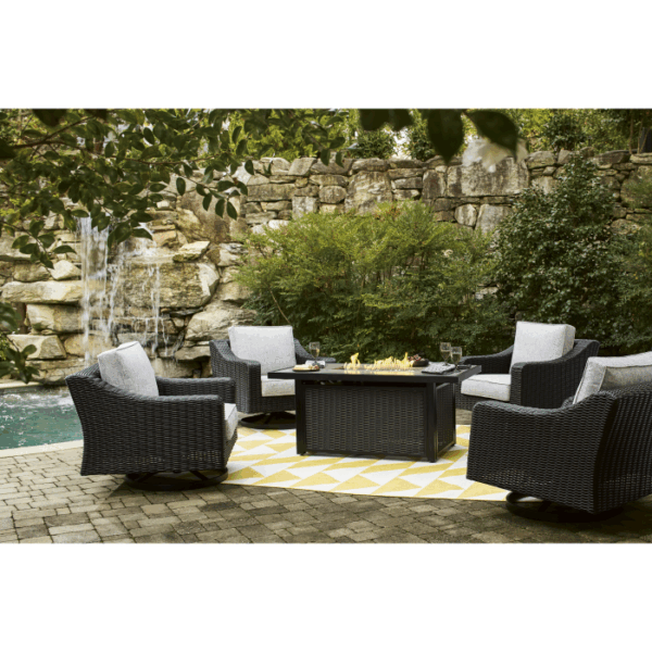The Beachcroft Deep Seating Firepit Set Black 5-piece features four wicker chairs with gray cushions around a rectangular fire pit table, arranged on a yellow and white rug atop a stone patio by a pool with rock waterfall and lush greenery.