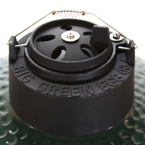 Close-up of the top vent of a BGE Small grill, featuring a black cast iron cap with adjustable slots, a spring handle, and “BIG GREEN EGG” engraved on the rim.