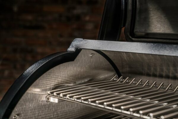 Close-up of a Timberline 1300 Pellet Grill featuring a shiny, clean grilling rack, with an out-of-focus brick wall in the background.