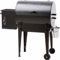 The TRAEGER-Pro Series 20 Blue wood pellet grill features a blue barrel-shaped lid, left-side control panel, two sturdy legs with wheels, and a small metal bucket on the right.