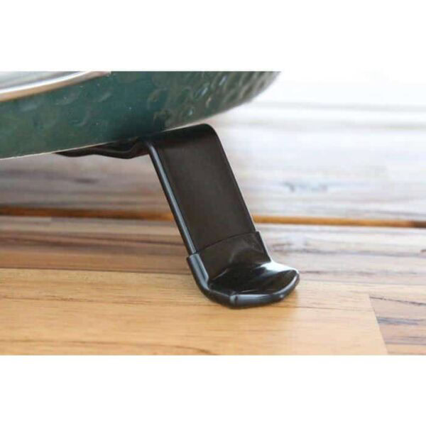 Close-up of the Table Nest for Large EGG, a black metal stand supporting the edge of a green grill on a wooden surface.