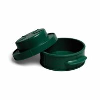 A dark green, round plastic Stuff-A-Burger Press with a matching lid, slightly tilted open to reveal the empty interior. The press features small side handles.