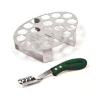 The Big Green Egg - Jalapeno Rack is a stainless steel rack with circular holes and a serrated, scoop-bladed green-handled tool, perfect for preparing and holding jalapeños or similar veggies for grilling.