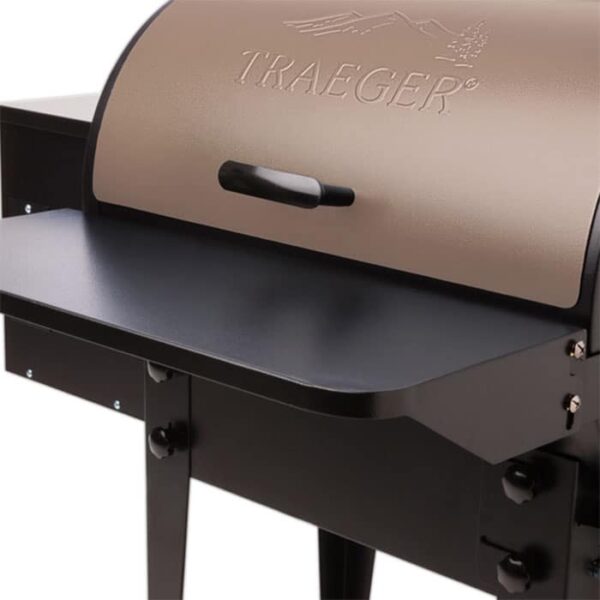 Close-up of a TRAEGER Folding Front Shelf-20 Series grill with a bronze lid, black handle, black side shelf, and the brand name embossed on the lid.