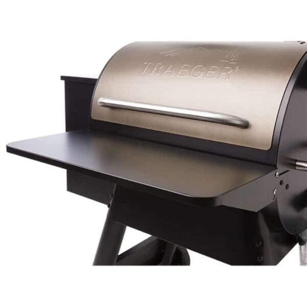Close-up view of a Traeger grill featuring the TRAEGER Folding Front Shelf-22 Series, with a stainless steel lid, large handle, and an attached black shelf providing extra workspace.