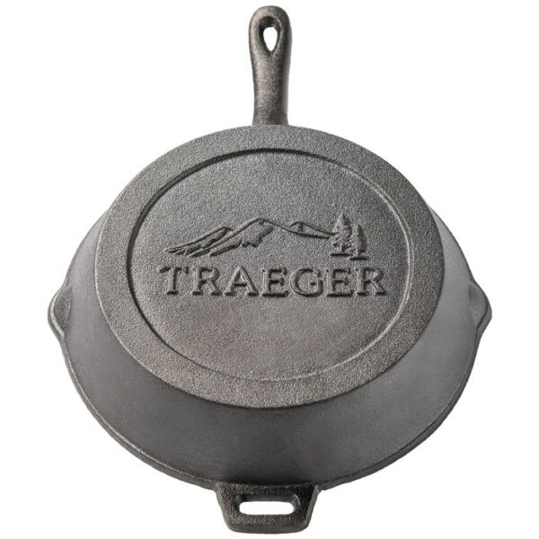 The TRAEGER 10.5 Cast Iron Skillet is shown from above, featuring an embossed Traeger logo and mountain design on the bottom, with a handle that includes a hole for hanging.