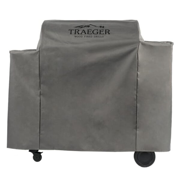 The Ironwood 885 Full-Length Grill Cover in gray, featuring the Traeger Wood Fired Grills logo, fits securely over a rectangular barbecue grill with two visible wheels at the base.