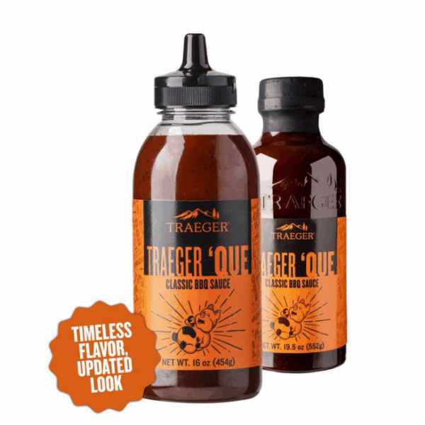 Two bottles of Traeger Que Savory BBQ Marinade 16 oz. are shown—one with a squeeze top, one with a screw cap and orange labels. A badge on the left reads Timeless Flavor, Updated Look.