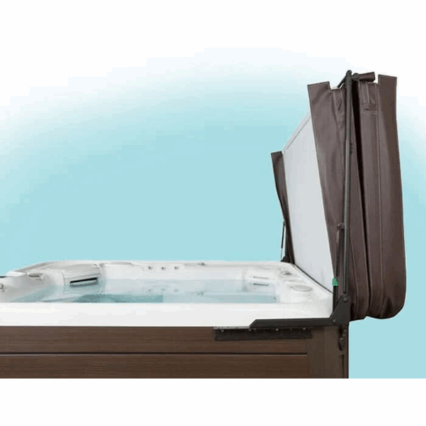 A brown and white hot tub with the Cover Lifter: Cover Valet Pro attached, displaying the cover partially lifted and supported vertically at the side against a blue and white backdrop.