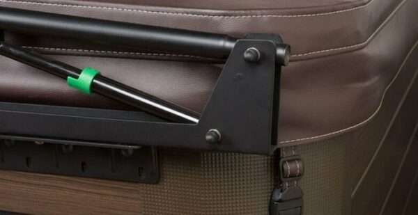 Close-up of the Cover Lifter: Cover Valet Pro attached to the corner of a brown hot tub, highlighting the metal support arm with a green clip and padded cover.