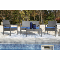 The Alina Grouping 4 piece features blue cushions, two chairs, a loveseat, and a coffee table with blue vases, all arranged on a striped rug beside a pool and surrounded by trees.