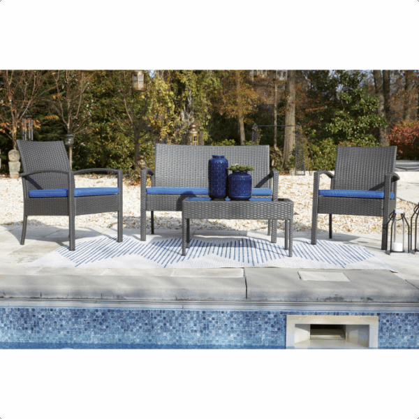 The Alina Grouping 4 piece features blue cushions, two chairs, a loveseat, and a coffee table with blue vases, all arranged on a striped rug beside a pool and surrounded by trees.
