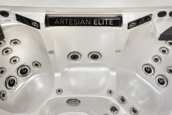 Close-up view of the inside of a Dove Canyon with Stereo hot tub in White Pearl Shell/Smoke Cabinet, featuring multiple water jets and a sign that reads ARTESIAN ELITE at the center.