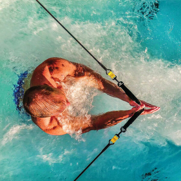A swimmer with outstretched arms dives into the blue water of the EP14 Swim Spa – Silver Marble Shell/Grey Cabinet, creating splashes as guide ropes line their entry.