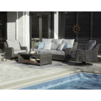 The Elite Park Grouping 4-piece includes gray wicker furniture: a sofa, two armchairs, and a coffee table with decor and pillows, all arranged on tile flooring beside a swimming pool.