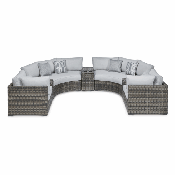 The Harbor Court Grouping 7-piece features a curved outdoor sectional sofa with light gray cushions, a rattan-style frame, matching center table, and decorative patterned throw pillows on the seats.