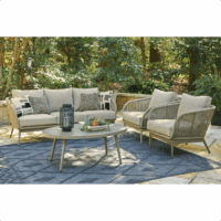 The Swiss Valley Grouping 5 piece features a cushioned sofa, two rope-detailed armchairs, and a round coffee table with accessories, all arranged on a blue rug in a lush garden.