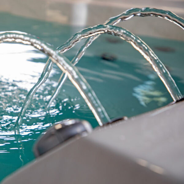 Close-up of arched water streams flowing into the EP12 Swim Spa with a Silver Marble Shell and Grey Cabinet Bench Seating, clear blue water, and part of the tub’s edge in view.