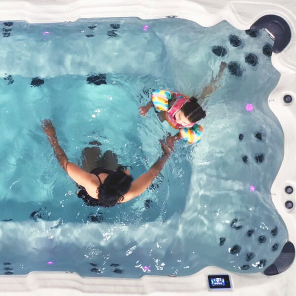 A woman and a young child wearing colorful floaties relax in an EP12 Swim Spa with a Silver Marble Shell and Grey Cabinet Bench Seating, seen from above as gentle ripples surround them.