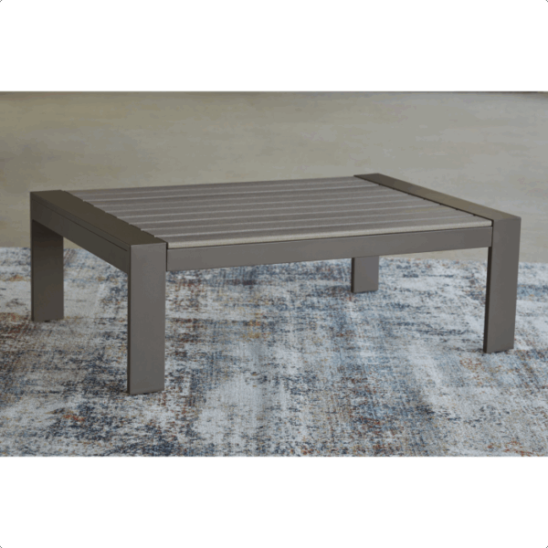 The Tropicava Grouping 4-piece features a modern, rectangular outdoor coffee table with a gray slatted top and sturdy metal legs, placed on a textured, multicolored rug.