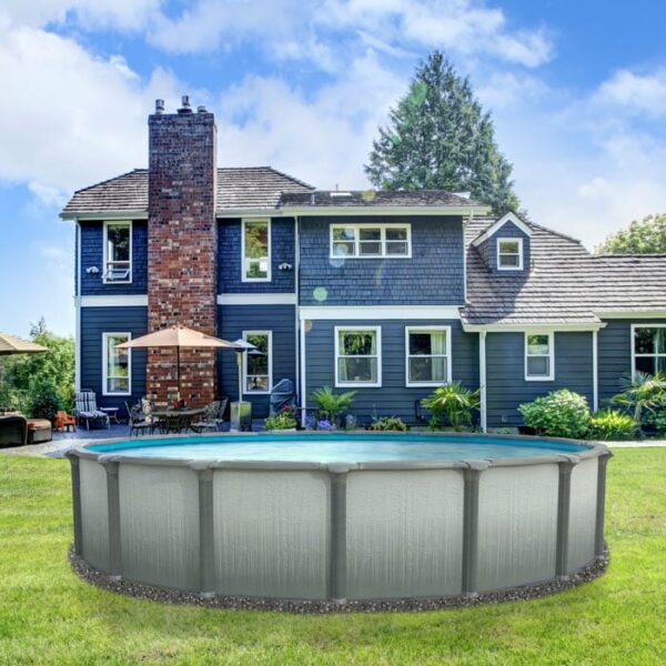 A 15 x 54 Serenity Pool Package is set up on the backyard lawn of a two-story blue house with a brick chimney, surrounded by patio furniture and green trees under a partly cloudy sky.